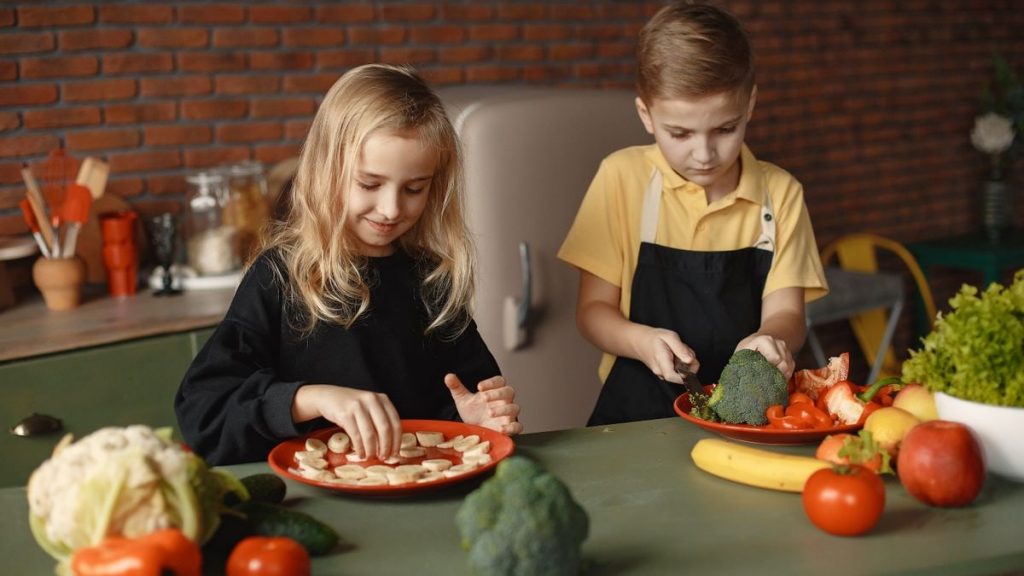 Two kids having fun preparing a healthy meal with fresh ingredients indoors.